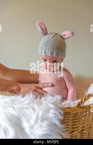 Bambino in maglia fatti in casa bunny ear hat seduta nel cesto di Pasqua con la divertente espressione facciale Foto Stock