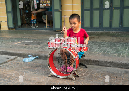 Un bambino che gioca i tamburi in una strada a Bangkok in Tailandia Foto Stock