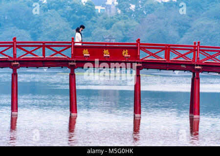 Una giovane coppia a piedi arcoss il celeberrimo dipinto di rosso Huc ponte sopra ho Lago Hoan Kiem, Hanoi, Vietnam che conduce al Den Ngoc Son Confucious Tempio. Foto Stock