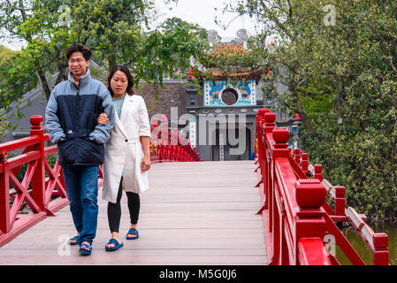 Una giovane coppia a piedi arcoss il celeberrimo dipinto di rosso Huc ponte sopra ho Lago Hoan Kiem, Hanoi, Vietnam che conduce al Den Ngoc Son Confucious Tempio. Foto Stock