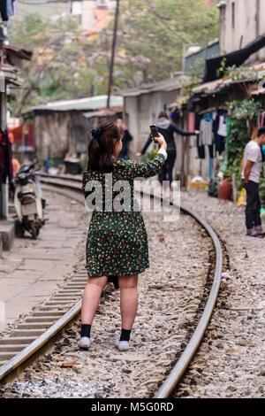 Un turista cinese prende un selfie su 'Hanoi Train Street', una strada stretta nel centro di Hanoi con binari ferroviari dal vivo su cui molte famiglie povere vivono, cucinano, mangiano e si lavano Foto Stock