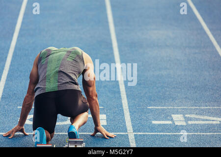 Vista posteriore di un atleta pronto a sprint su un all-weather via di corsa. Runner utilizzando un blocco di partenza per iniziare la sua esecuzione sulla pista. Foto Stock