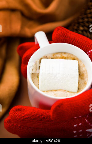 Vista ravvicinata della persona con i guanti rossi di prendere una tazza di cioccolata calda con marshmallow Foto Stock
