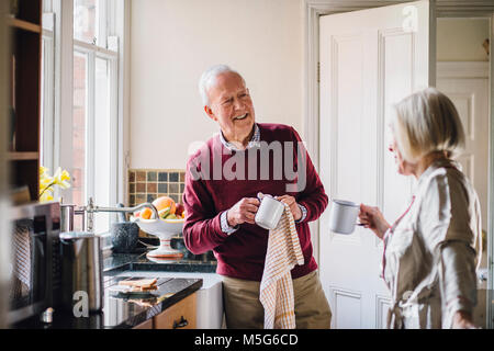 Senior l uomo sta parlando con sua moglie in cucina. Egli è l'asciugatura delle stoviglie e la donna è dirnking tè. Foto Stock