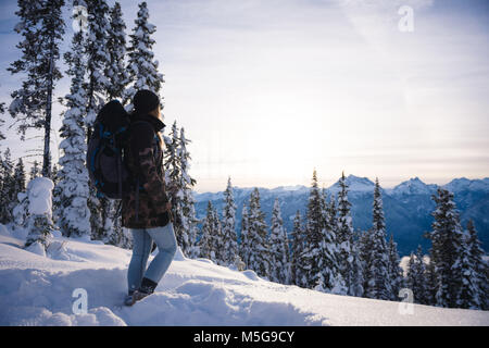 Donna con zaino guardando montagne coperte di neve e di pino Foto Stock