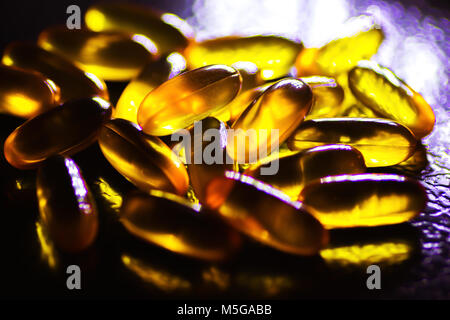 Olio di fegato di merluzzo pillole in luce posteriore bakground scuro Foto Stock