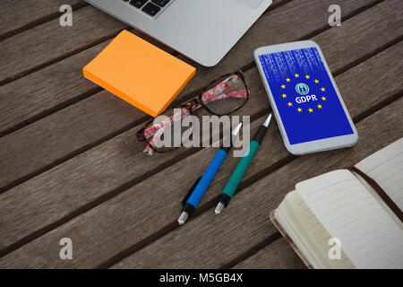 Immagine composita del telefono mobile, laptop, penna, nota adesiva, occhiali e agenda elettronica sul tavolato in legno Foto Stock