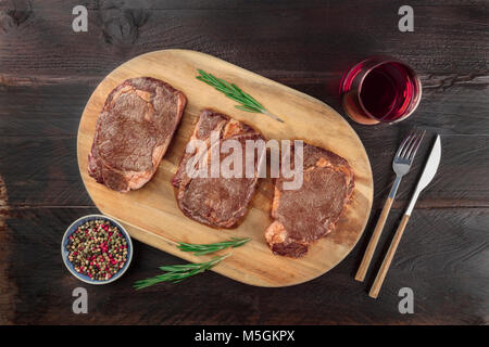 Una foto aerea di tre fette di carne cotta, filetti di manzo, ripresa dall'alto sul buio rustica con rametti di rosmarino, sale, pepe, vino, Foto Stock