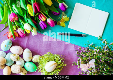 Felice Pasqua Primavera colpo da sopra come flatlay con notebook vuota con la penna per il messaggio e tulipani colorati, fiori e uova di pasqua Foto Stock