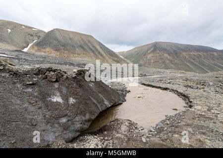 La fine del ghiacciaio. Un fiume marrone, l'acqua di disgelo dal ghiacciaio Longyear, proveniente da sotto il ghiaccio. Longyear Valley. Paesaggio artico di morena glaciale di pietre e montagne, isole Svalbard. Foto Stock