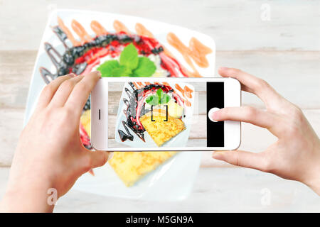 Immagine composita di realizzare foto culinarie su uno smartphone - donna di mani tenendo il telefono cellulare e toccando il pulsante otturatore sullo schermo. Foto Stock