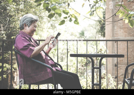 Asian elder donna tenendo il telefono cellulare sulla terrazza. anziani femmina messaggio sms, utilizzando app con lo smartphone sul patio. senior di usare il cellulare per connettersi Foto Stock