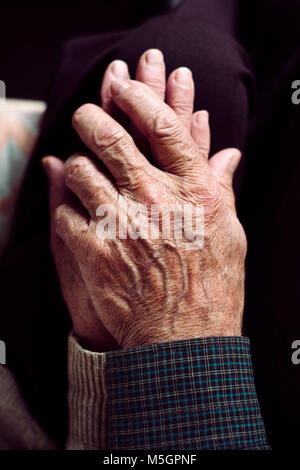 Elevato angolo di visione di un vecchio uomo caucasico e un vecchio caucasian donna seduta in un lettino tenendo le mani con affetto Foto Stock