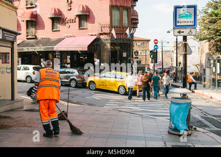 Bidello in arancio luminoso uniforme di spazzare la piastrella sulla strada nel quartiere di Sultanahmet ad Istanbul in Turchia. Pedoni che attraversano la strada in bac Foto Stock