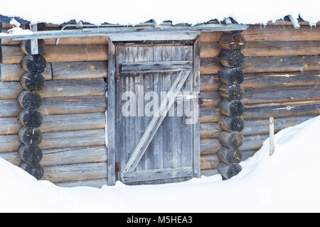 Piccola casa in legno ricoperta di neve e circondato da una natura invernale. Foto Stock
