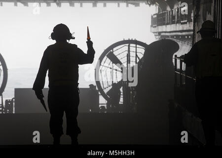 Un U.S. Navy Sailor con l'Iwo Jima Amphibious Ready Group (ARG), i segnali a Landing Craft Air Cushion (LCAC) di discostarsi ben coperta dell'assalto anfibio nave USS Iwo Jima (LHD 7), 11 febbraio, 2018. L'ARG/26 Marine Expeditionary Unit (MEU) team è la distribuzione in mare per condurre le operazioni di sicurezza marittima, di risposta alla crisi e al teatro la cooperazione in materia di sicurezza, fornendo anche una marcia di avanzamento expeditionary presenza navale in Europa e in Medio Oriente. (U.S. Marine Corps Foto Stock