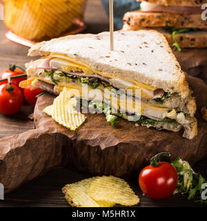 Nuovo club sandwich con prosciutto e formaggio, uova sode e patate chips su sfondo di legno. Un sano fast food concept. Foto Stock