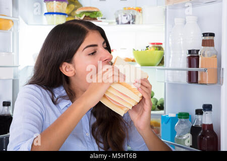 Close-up di una giovane donna di mangiare panino in parte anteriore del frigorifero Foto Stock