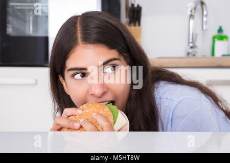 Close-up di una giovane donna segretamente mangiare hamburger a casa Foto Stock