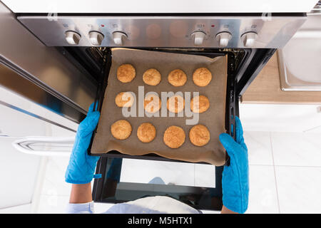 Angolo di Alta Vista di una mano umana tenendo fuori il vassoio di biscotti dal forno Foto Stock