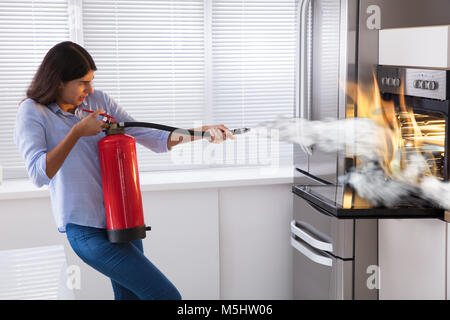 Giovane donna con un estintore per spegnere un incendio dal forno a casa  Foto stock - Alamy