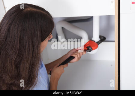 Close-up di giovane donna dissipatore di serraggio canalizzazione Con Monkey Wrench in cucina Foto Stock