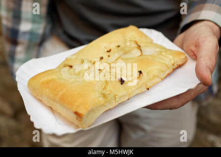 Uomo in possesso di un vassoio della carta con una fetta di cipolla focaccia, tradizionale pane italiano Foto Stock