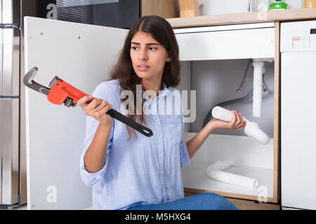 Giovane donna dissipatore di contenimento tubo e Monkey Wrench in cucina Foto Stock