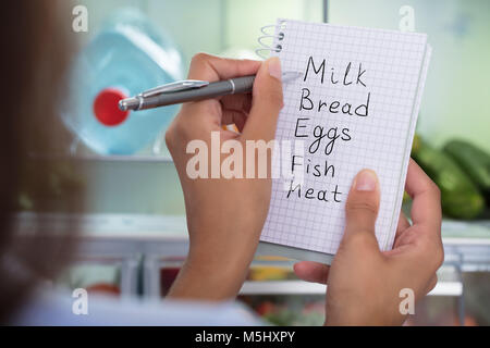 Close-up di donna azienda libro a spirale con Check List contro il frigorifero aperto a casa Foto Stock