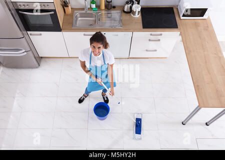 Donna felice pulizia pavimento con Mop in cucina a casa Foto Stock