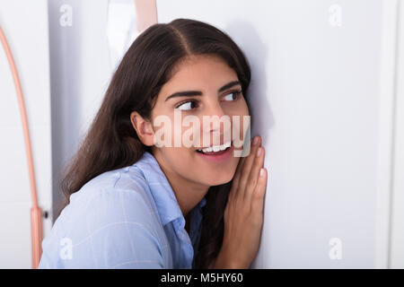 Close-up di curioso giovane donna ascoltare attentamente attraverso la parete Foto Stock