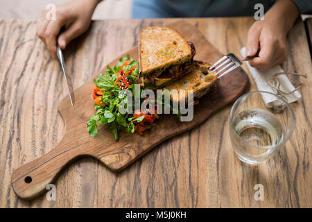 Mani tenendo il coltello e la forchetta al tavolo di legno decorate con insalata e pane croccante Foto Stock