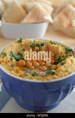 Hummus rabboccato con tutto i ceci, il prezzemolo e l'olio d'oliva nella ciotola blu contro le fette di pane pita Foto Stock