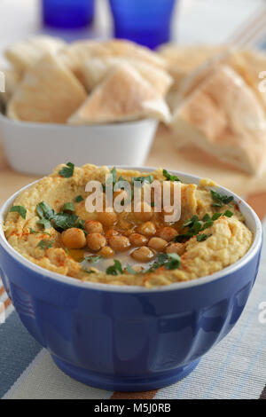 Hummus rabboccato con tutto i ceci, il prezzemolo e l'olio d'oliva nella ciotola blu contro le fette di pane pita Foto Stock