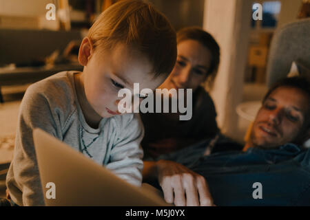 La famiglia tramite computer portatile sul lettino al buio Foto Stock