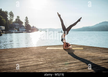 La donna a praticare yoga sul pontile di un lago Foto Stock