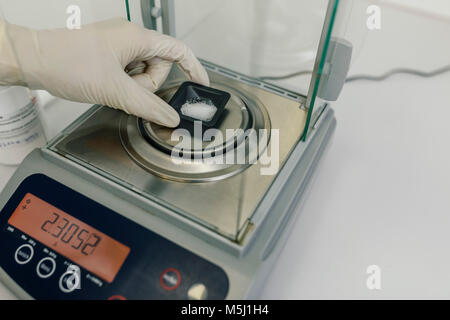 Mano con guanto protettivo utilizzando scale in laboratorio di una farmacia Foto Stock