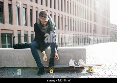 Libero professionista con longboard seduta sul banco la legatura le sue scarpe Foto Stock