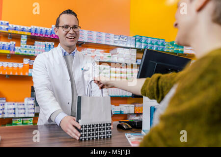 Il farmacista dando borsa con la medicina per il cliente in farmacia Foto Stock