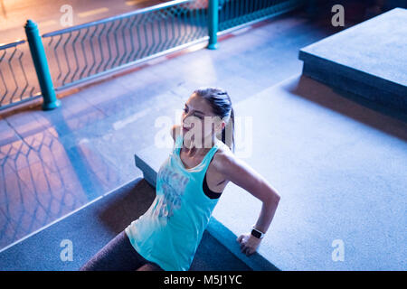 Giovane donna facendo retromarcia pushups nel moderno impianto urbanistico di notte Foto Stock