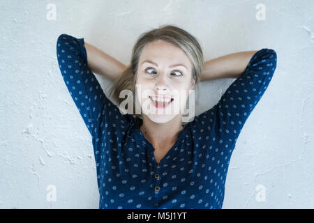 Ritratto di giovane donna sdraiata sul pavimento tirando funny faces Foto Stock