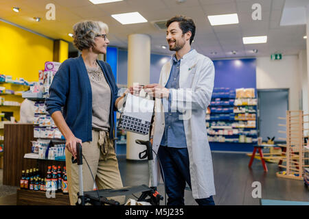 Il farmacista dando borsa di medicina per il cliente con scuotipaglia con ruote in farmacia Foto Stock