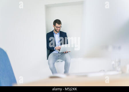 Imprenditore sorridente seduto in una nicchia con laptop Foto Stock