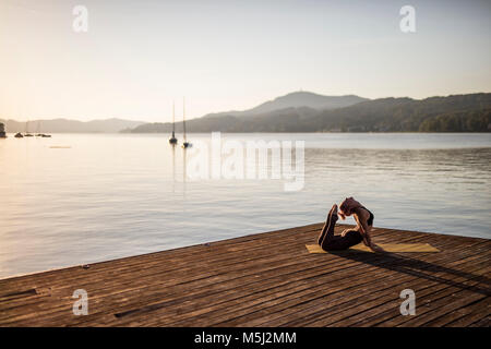La donna a praticare yoga sul pontile di un lago Foto Stock