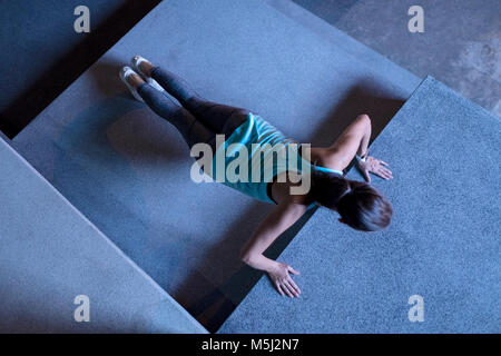 Giovane donna fa pushups nel moderno impianto urbanistico di notte Foto Stock