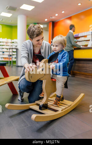 Little Boy e madre giocando con il cavallo a dondolo in farmacia Foto Stock