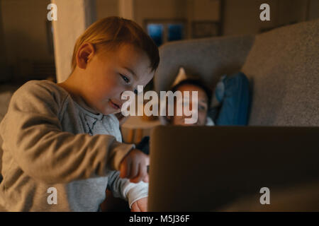 Poco ragazza con i genitori guardando il laptop sul lettino al buio Foto Stock