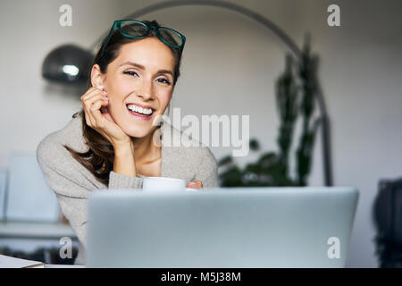 Ritratto di felice giovane donna a casa con il computer portatile Foto Stock