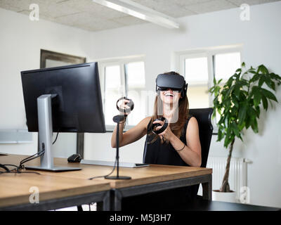 Donna felice indossando occhiali VR alla scrivania in ufficio Foto Stock