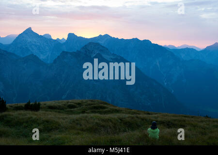 Austria, Tirolo, escursionista seduta nel prato alpino al crepuscolo Foto Stock